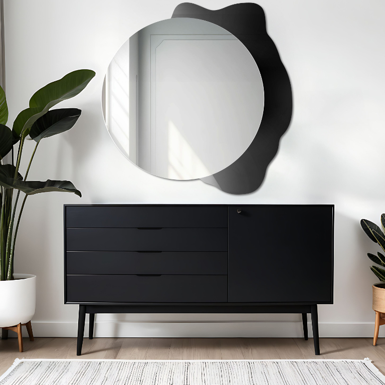Dekoratives rundes Spiegelmodell Plamko mit organisch geformtem Dekor über einer schwarzen Kommode, ergänzt durch grüne Zimmerpflanzen und dezente Einrichtungselemente im minimalistischen Stil.